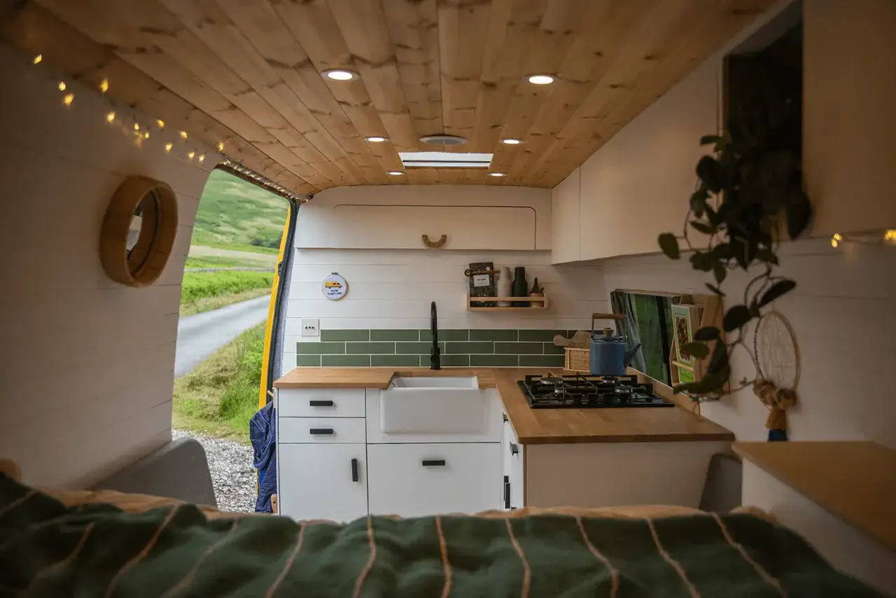 Cocina funcional y acogedora en una furgoneta camper. La distribuci&oacute;n furgoneta camper optimiza el espacio con encimera, fregadero, cocina y almacenamiento.