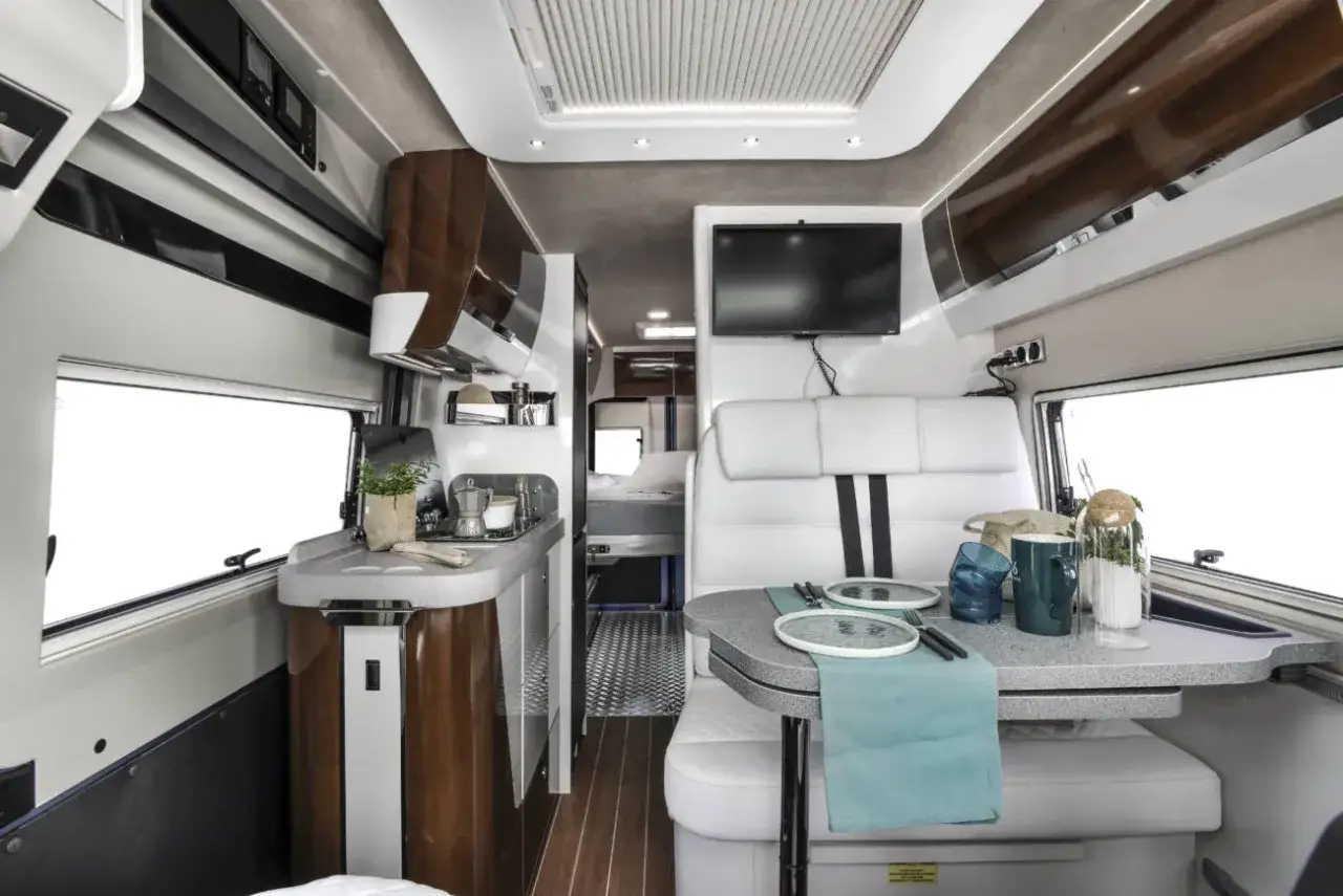 Interior de un autocar vivienda moderno y elegante, con cocina equipada, zona de comedor y asientos de cuero blanco.
