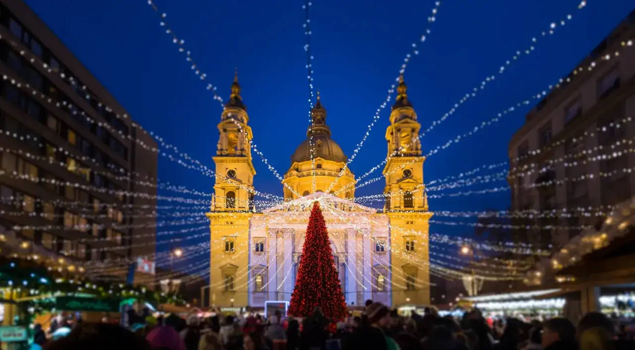 Mercado navideño en Budapest con árbol rojo y luces festivas frente a la basílica.