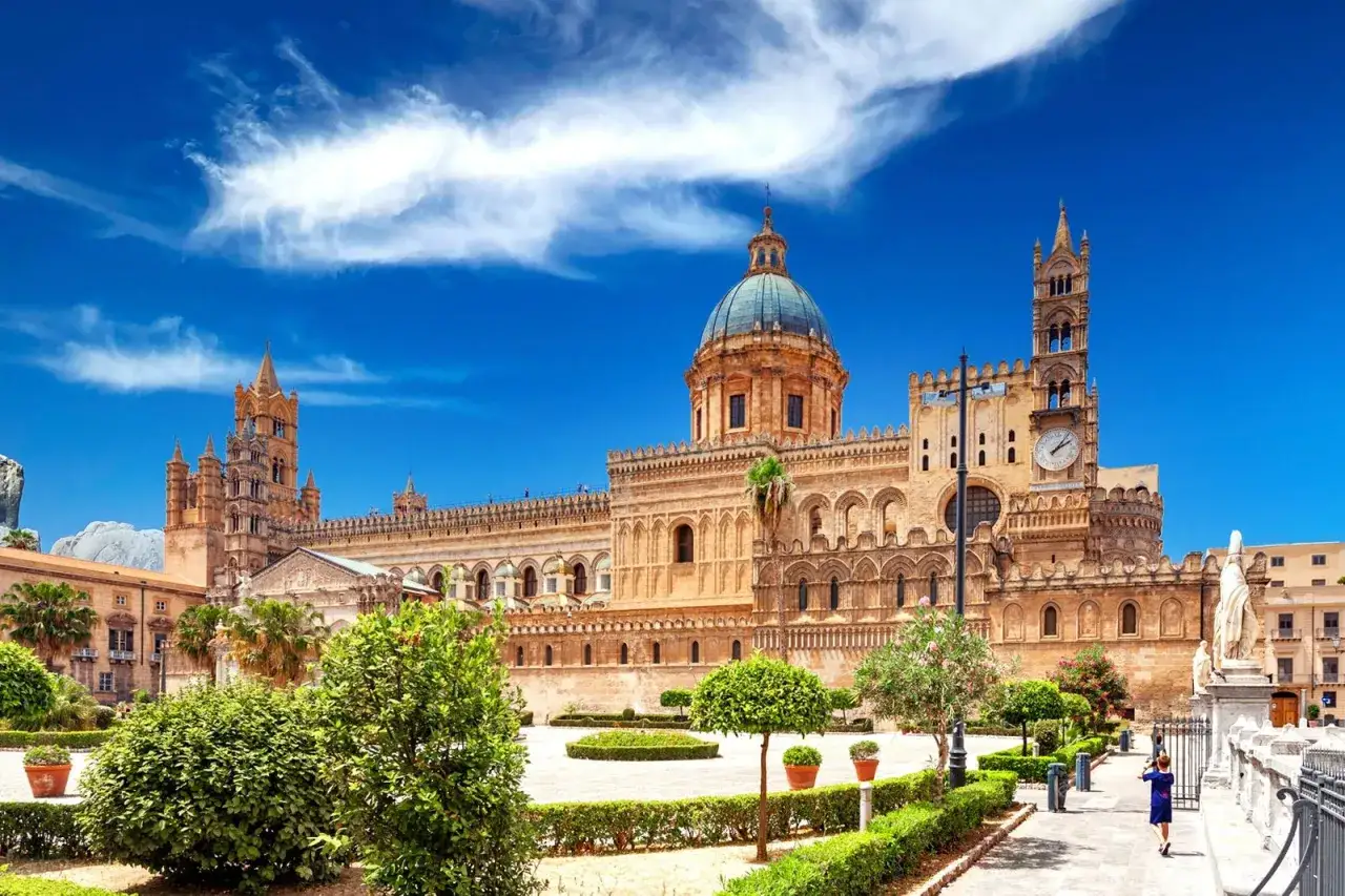 La Catedral de Palermo, imponente y majestuosa, se alza bajo un cielo azul vibrante. A pesar de su belleza, se rumorea que Palermo peligroso es solo un mito, pues la historia y la arquitectura cautivan.