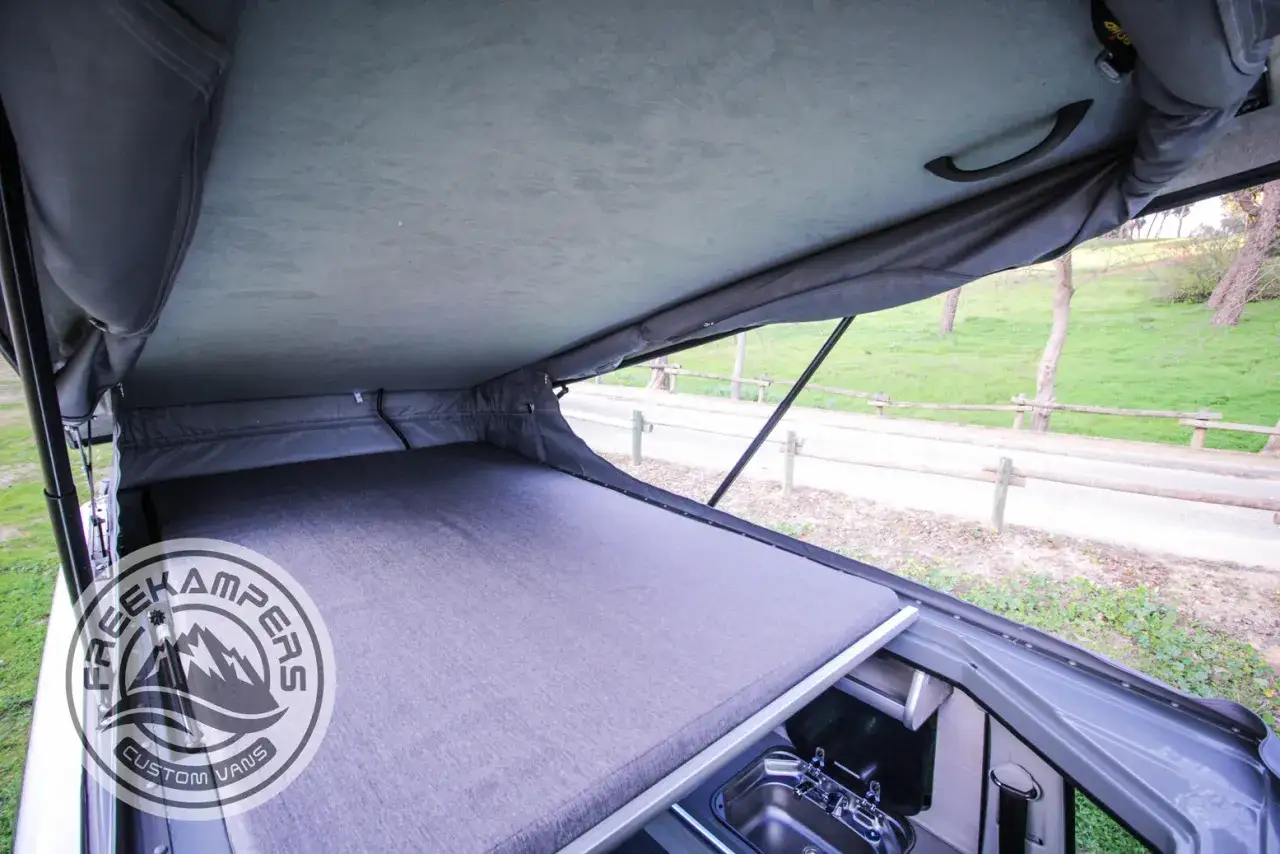 Interior de furgoneta camper con cama y techo elevable abierto. Ideal para elevar techo furgoneta y disfrutar del espacio.