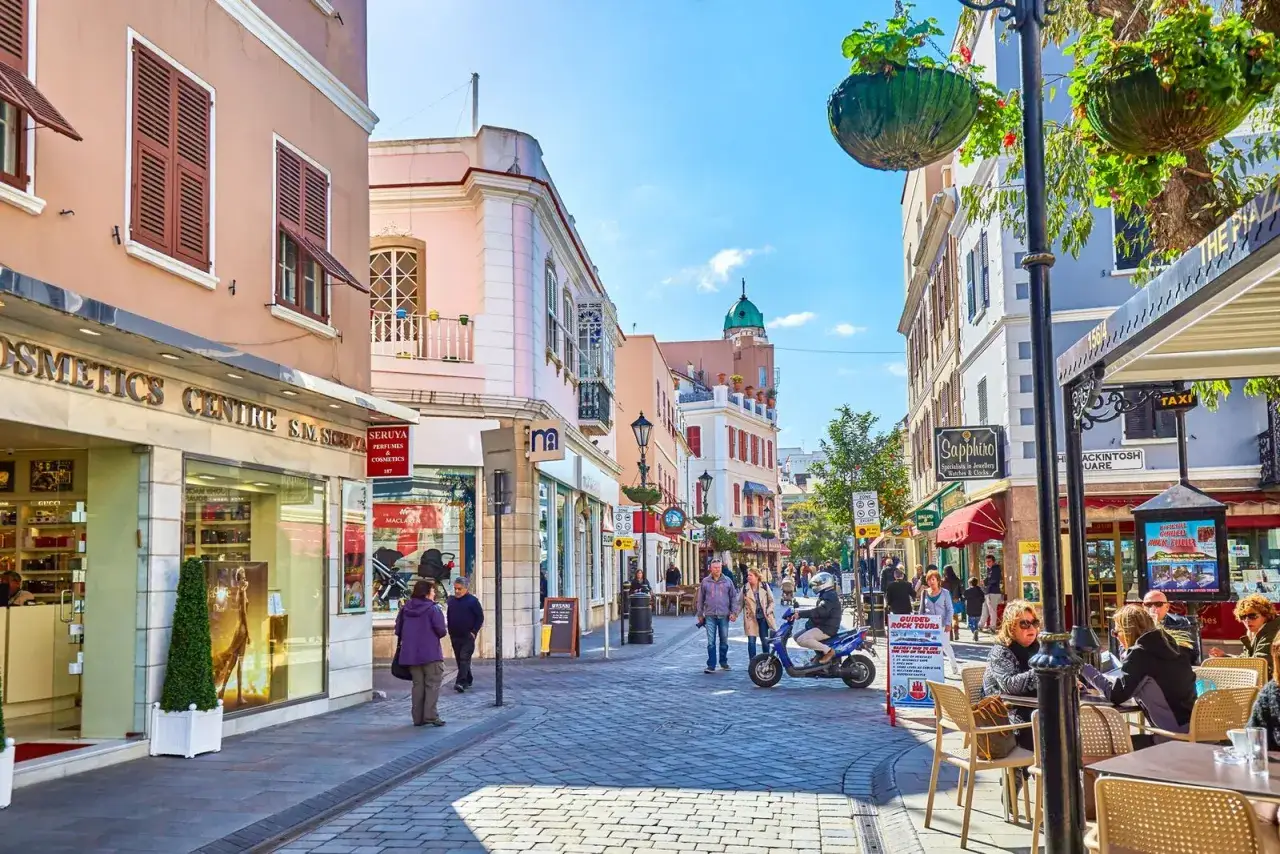 Calle peatonal con tiendas y gente disfrutando de un d&iacute;a soleado. Ideal para visiter Gibraltar a pie y descubrir sus encantos.