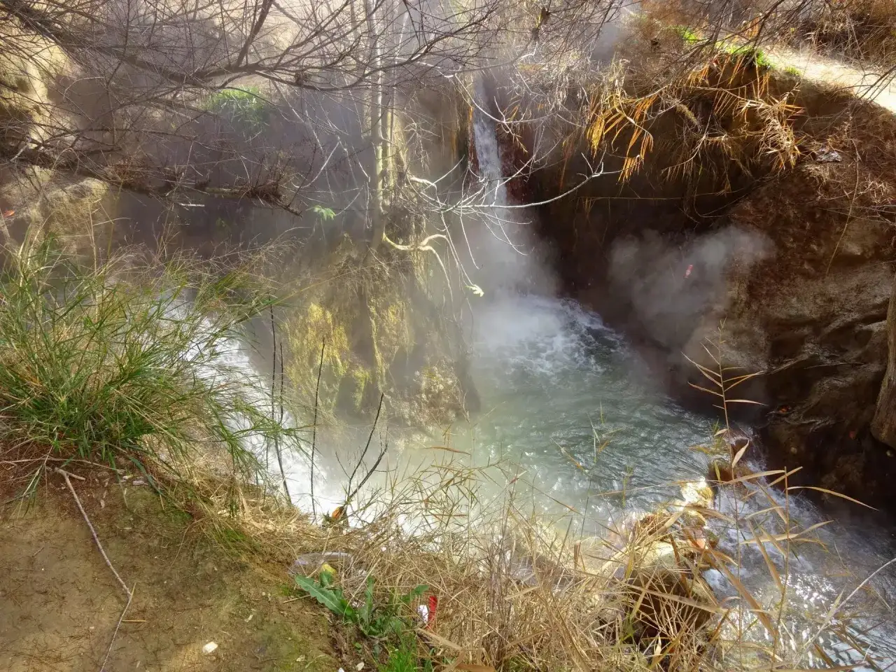 Vapor ascendente de las aguas termales Santa Fe, un remanso natural con vegetaci&oacute;n y rocas.