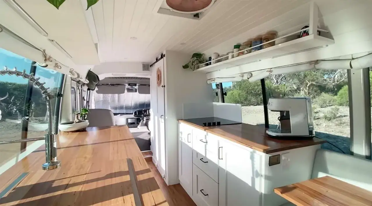 Interior de un minibus vivienda con cocina completa, cafetera y grifo de diseño.