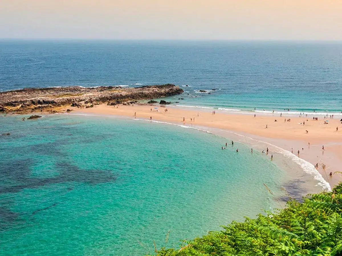 La playa de la rabia se extiende con arena dorada y aguas turquesas. Personas disfrutan del sol y el mar en este id&iacute;lico paisaje costero.