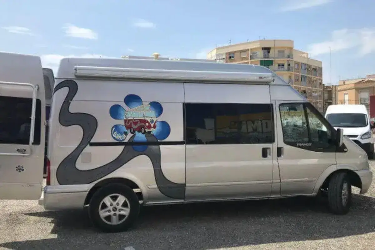 Furgoneta camperizada con motor Ford 2.2 TDCI 140 CV, decorada con un dise&ntilde;o de carretera y una flor con una furgoneta retro.
