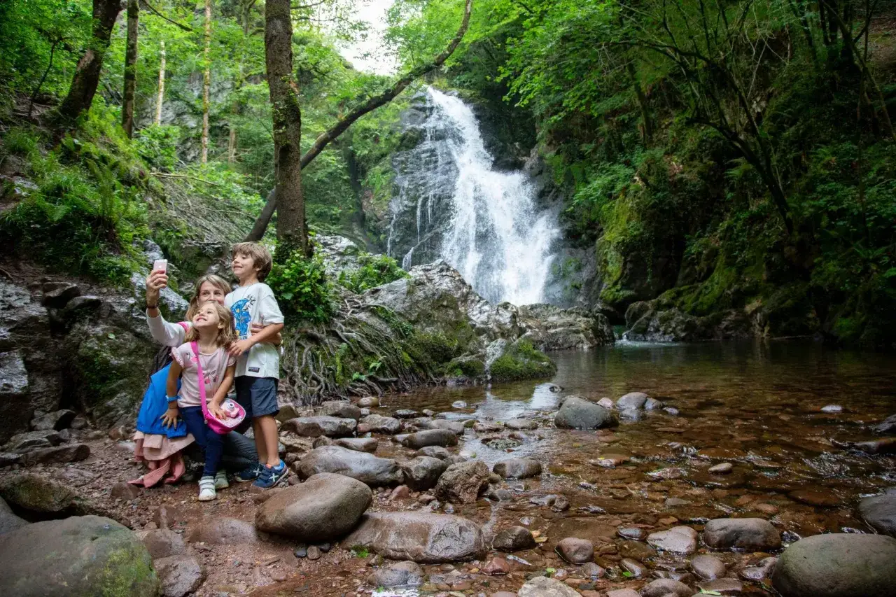 Familia se toma una selfie frente a la imponente cascada Txorrotxin, rodeada de exuberante vegetaci&oacute;n y rocas.