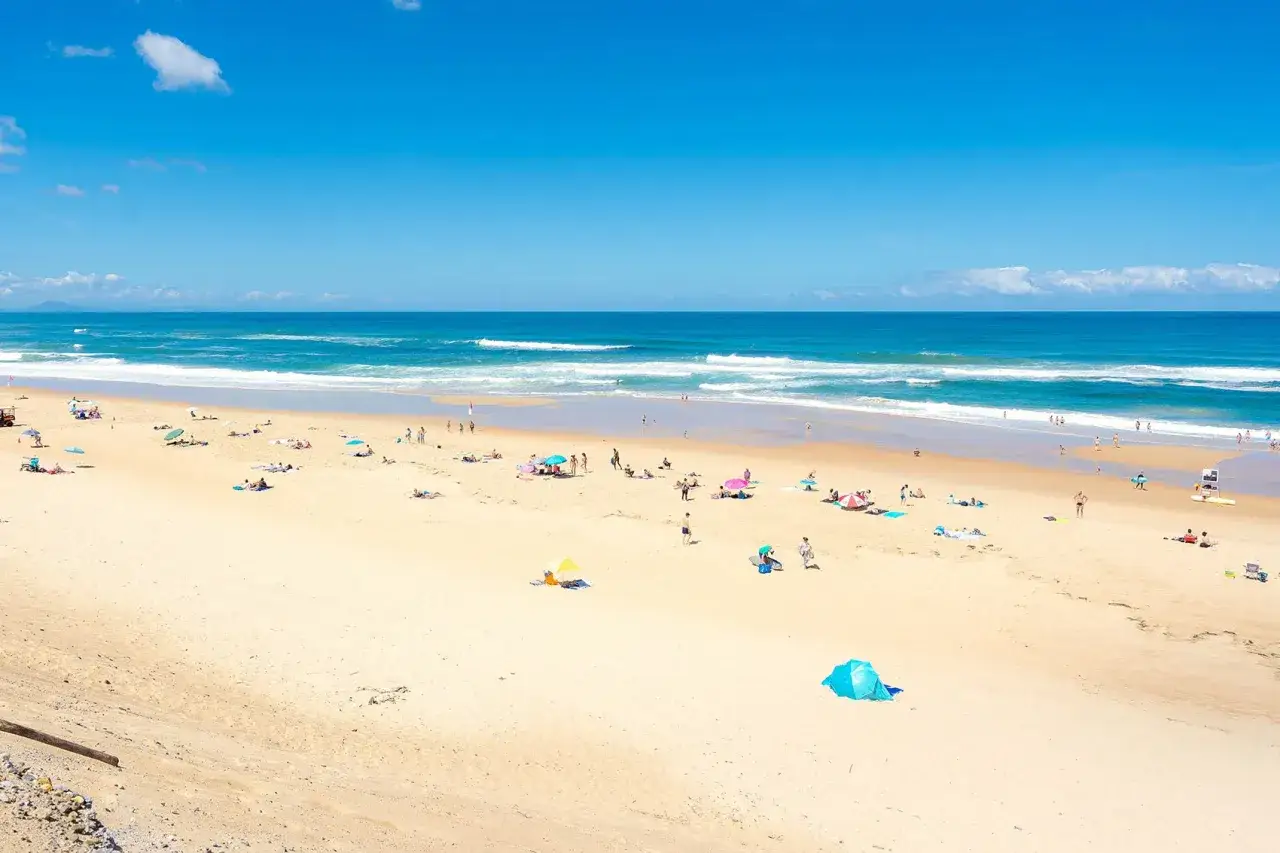 Gente disfrutando del sol y el mar en las landas playas. Olas azules y arena dorada bajo un cielo despejado.