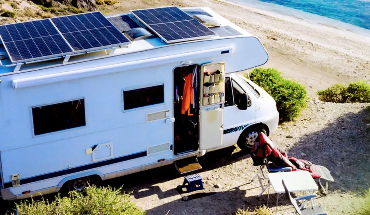 Autocaravana con instalaci&oacute;n de placas solares y bater&iacute;as, lista para una aventura sostenible junto al mar.
