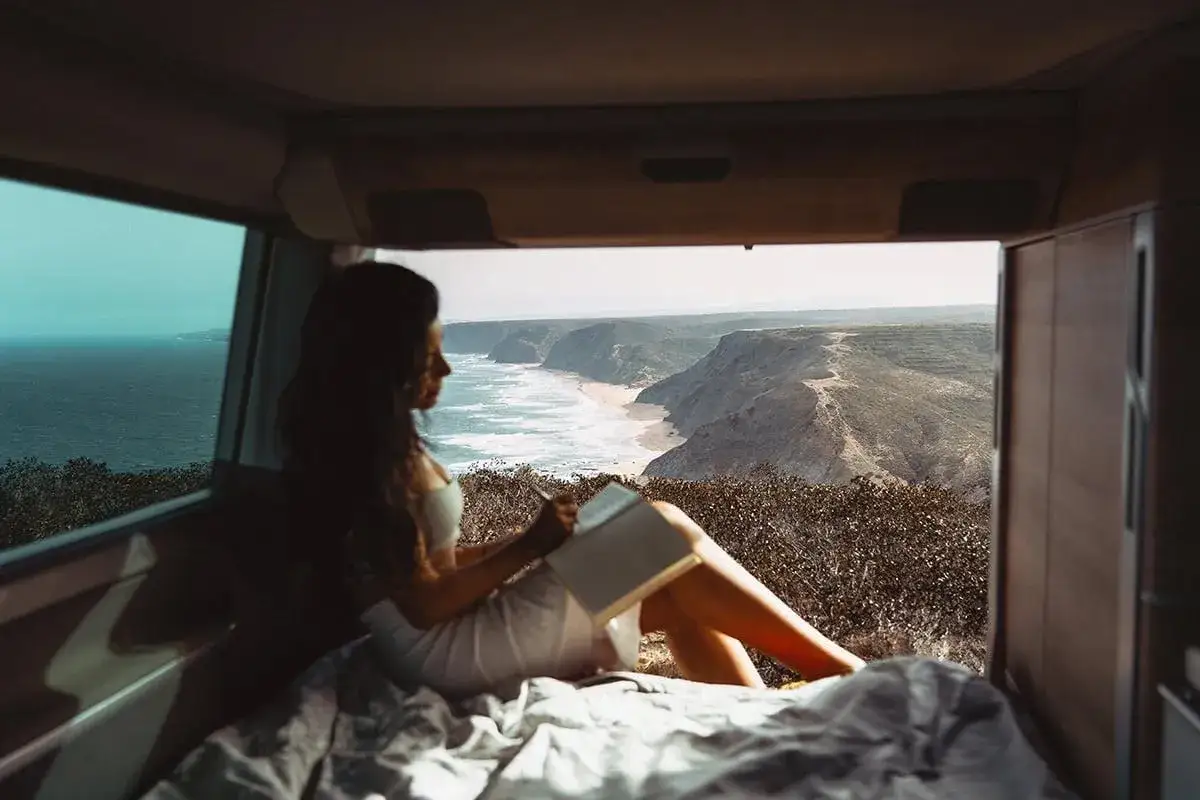 Mujer leyendo en su autocaravana con vistas al mar y acantilados del sur de Portugal.