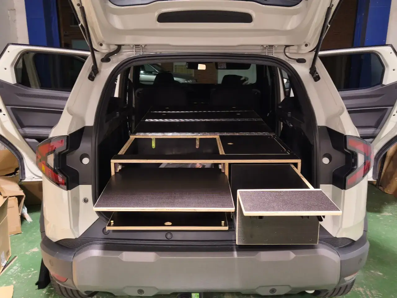 Interior de un suv camper con m&oacute;dulos de madera para almacenamiento y cama.