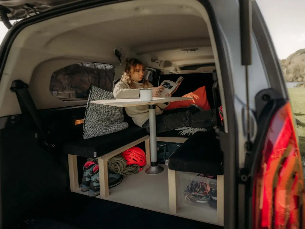 Interior de Ford Tourneo Courier camperizada. Mujer leyendo, equipamiento de monta&ntilde;a y almacenamiento optimizado.