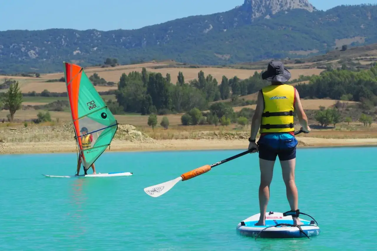 Un d&iacute;a soleado en el pantano de Alloz. Windsurf y paddle surf en aguas turquesas, con monta&ntilde;as verdes de fondo.
