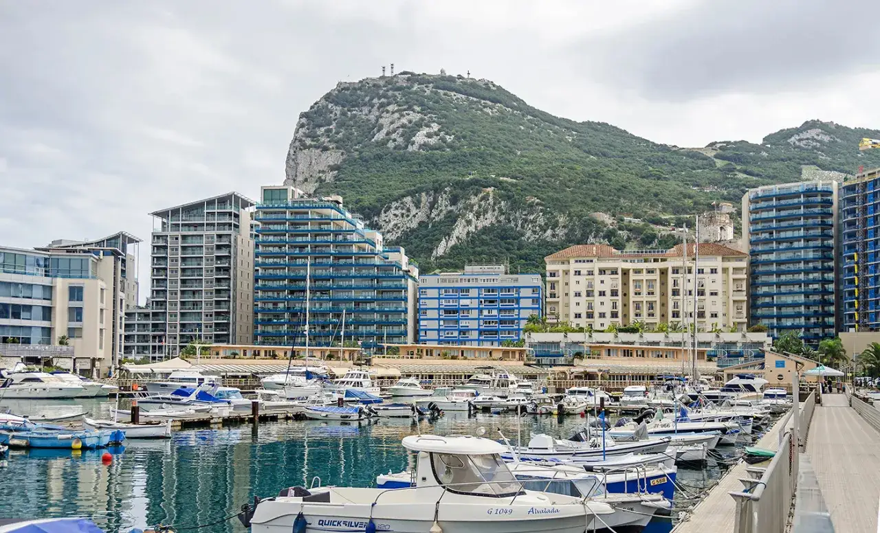 Puerto deportivo con yates y edificios modernos, con el Pe&ntilde;&oacute;n de Gibraltar al fondo. Ideal para saber dove parcheggiare a Gibilterra.