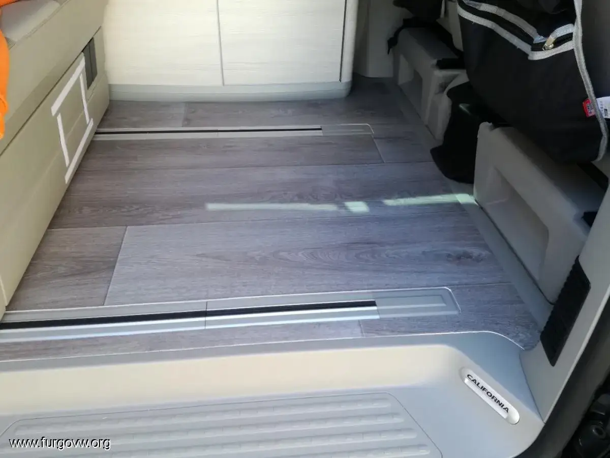 Suelo de autocaravana con acabado de madera gris, ideal para forrar suelo con vinilo. Se ve el riel de la puerta corredera.