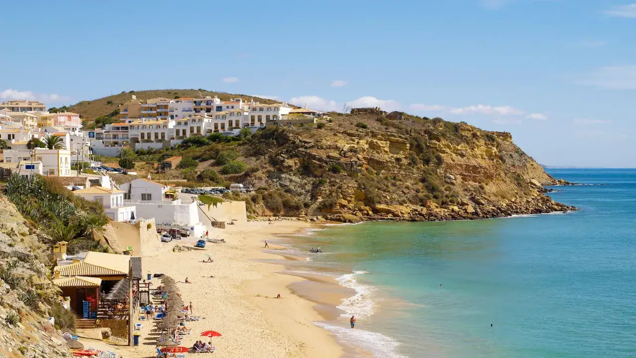 La praia do Burgau se despliega con arena dorada, aguas turquesas y casas blancas en la ladera. Un d&iacute;a perfecto para disfrutar del sol y el mar.