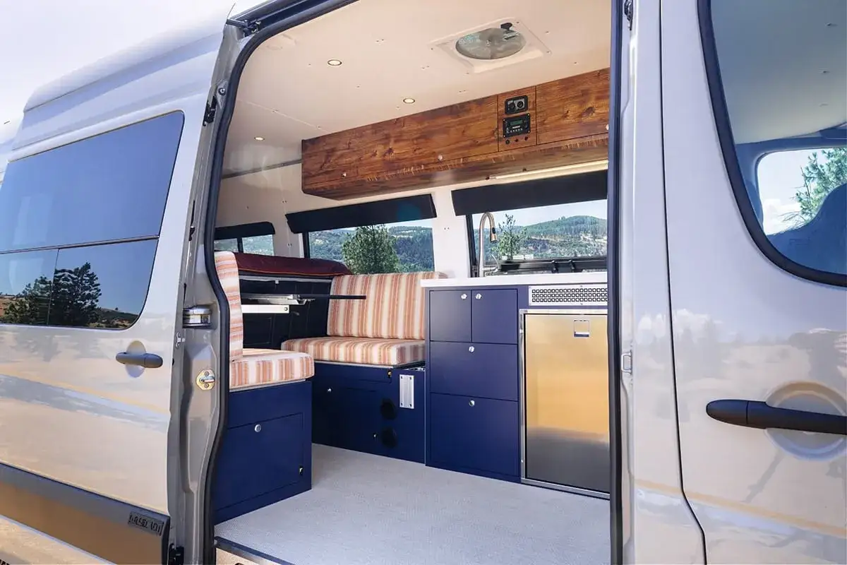 Interior de una autocaravana con asientos a rayas, cocina y nevera. Un ejemplo perfecto de cómo transformar autobuses en acogedoras autocaravanas.