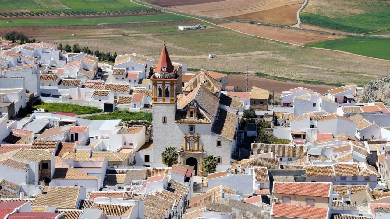 Vista a&eacute;rea del pintoresco pueblo teba, con casas blancas y tejados de teja, dominado por una iglesia con campanario.