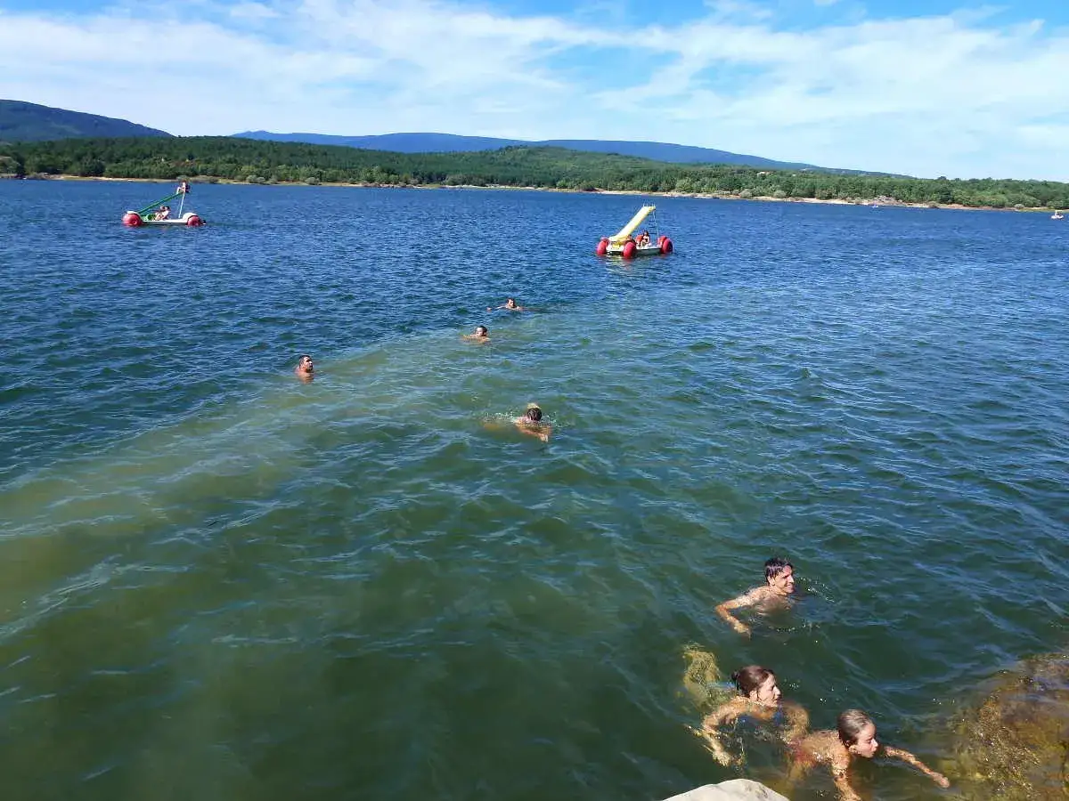 Gente nadando en un lago azul, con botes de pedales y colinas verdes al fondo. &iexcl;Un d&iacute;a perfecto para visitar la playa pita como llegar!