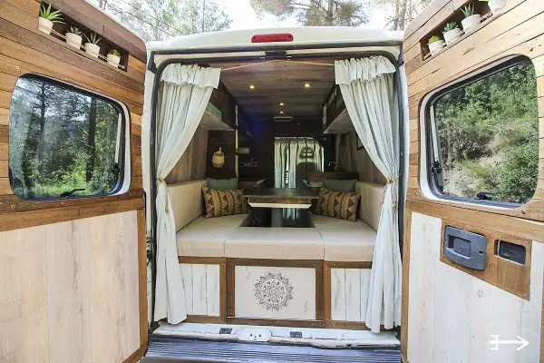 Interior de una caravana camperizada con asientos, mesa y decoración rústica. ¡Perfecta para aventuras!