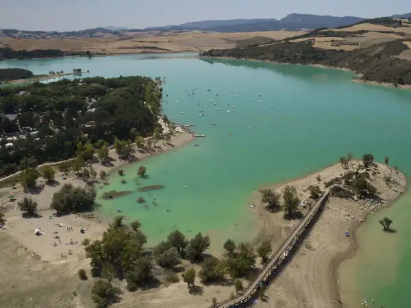 El pantano de Alloz, con sus aguas turquesas, acoge veleros y bañistas. Un puente de madera conecta la orilla con una pequeña isla.