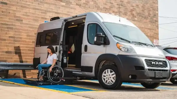Mujer en silla de ruedas desciende de un minibus vivienda con rampa accesible.