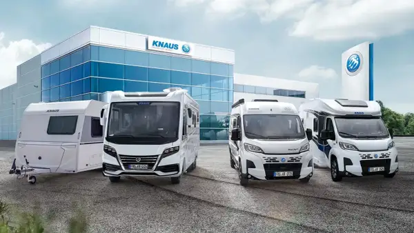Una caravana y tres autocaravanas KNAUS blancas frente a un edificio moderno.