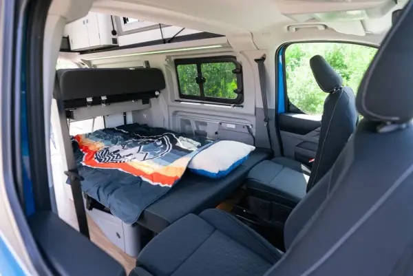 Interior del Ford Nugget con cama lista para dormir, cojín y asientos delanteros.