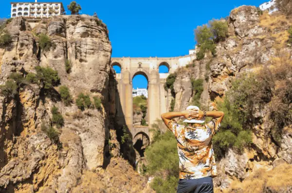 Un hombre con sombrero blanco admira el Puente Nuevo de Ronda en un día soleado.