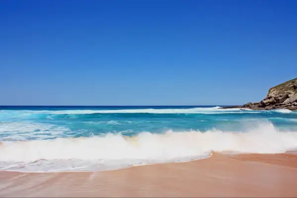 Olas rompiendo en una playa de arena dorada, ideal para saber donde hacer snorkel en Cantabria. Cielo azul intenso.