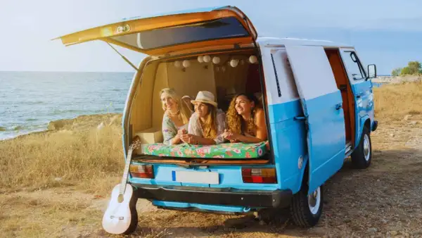 Tres amigas disfrutan de la vida en su furgoneta camperizada junto al mar. Inspiración para saber como camperizar una furgoneta.