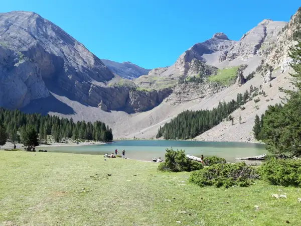 Ibón de Plan con montañas, bosque y gente en la orilla.
