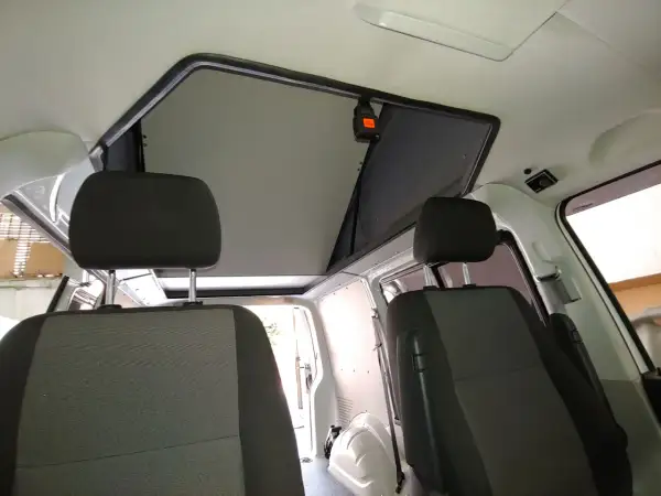 Interior de furgoneta con asientos delanteros y un techo elevable abierto, listo para la aventura.