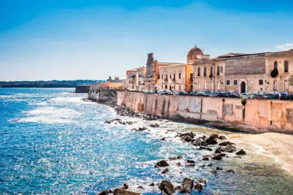 Costa de Siracusa, Sicilia, con edificios históricos y el mar azul brillante.