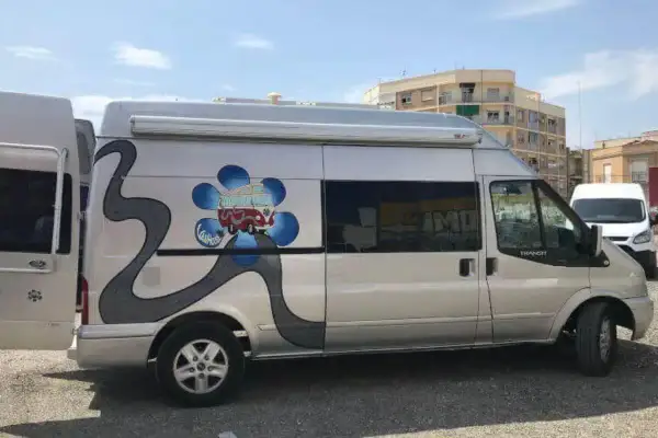 Furgoneta camperizada con motor Ford 2.2 TDCI 140 CV. Decoración de flor azul y carretera gris.