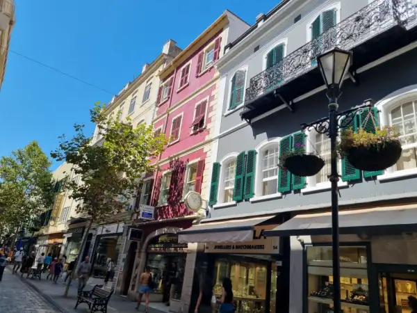 Edificios coloridos y tiendas en la Gibraltar altstadt, con gente paseando bajo un cielo azul brillante.