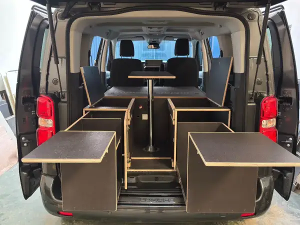 Soluciones de trucos almacenaje furgonetas camper: módulos de madera con compartimentos y mesa abatible para maximizar el espacio.