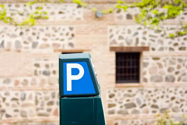 Parquímetro azul con letra P blanca, señalando opciones de altstadt Marbella parken. Edificio de piedra y ladrillo al fondo.