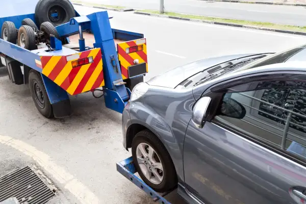 Grúa azul lista para transportar caravana. El coche gris está asegurado en la plataforma.