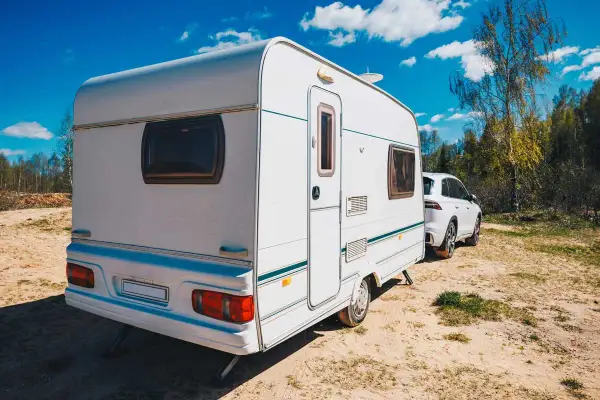 Caravana blanca lista para el transporte, aparcada junto a un coche en un día soleado.