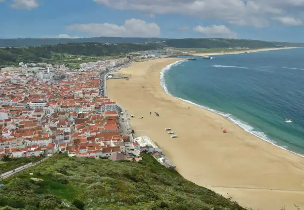 Vista aérea de Nazaré, Portugal, con su extensa playa dorada y el mar azul. Planifica tu viaje a Nazaré, Portugal, como llegar es fácil.